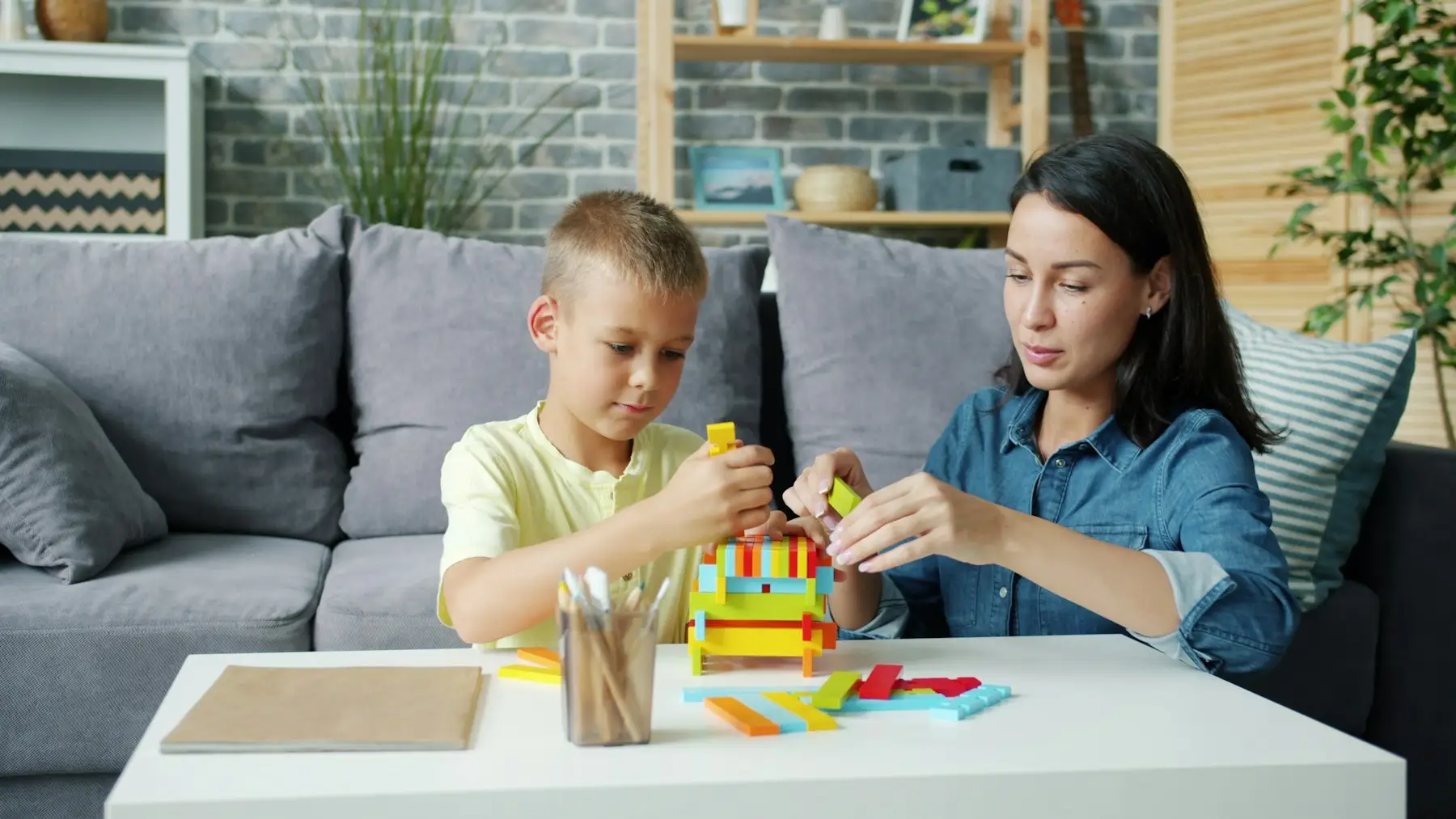 Mãe e filho montando juntos uma torre de blocos coloridos na mesa da sala