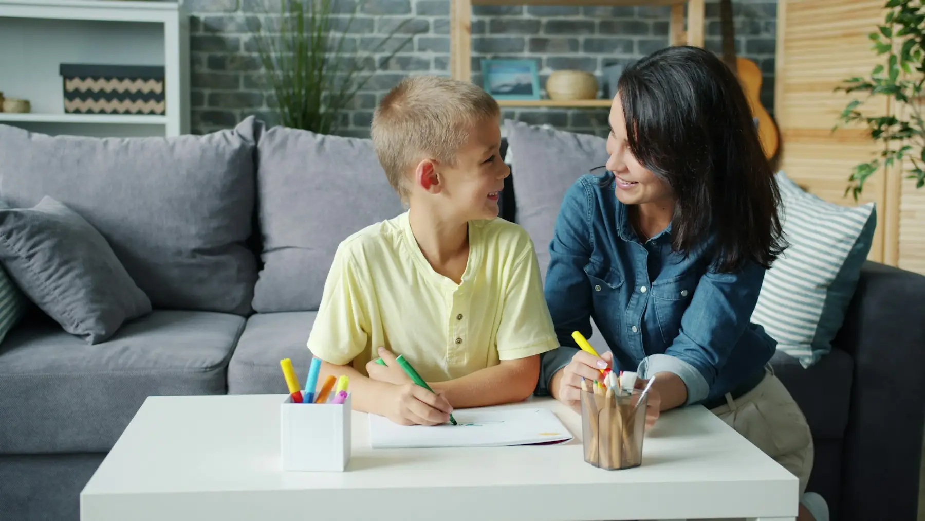 Mãe e filho desenhando juntos em uma mesa de centro, na sala de casa