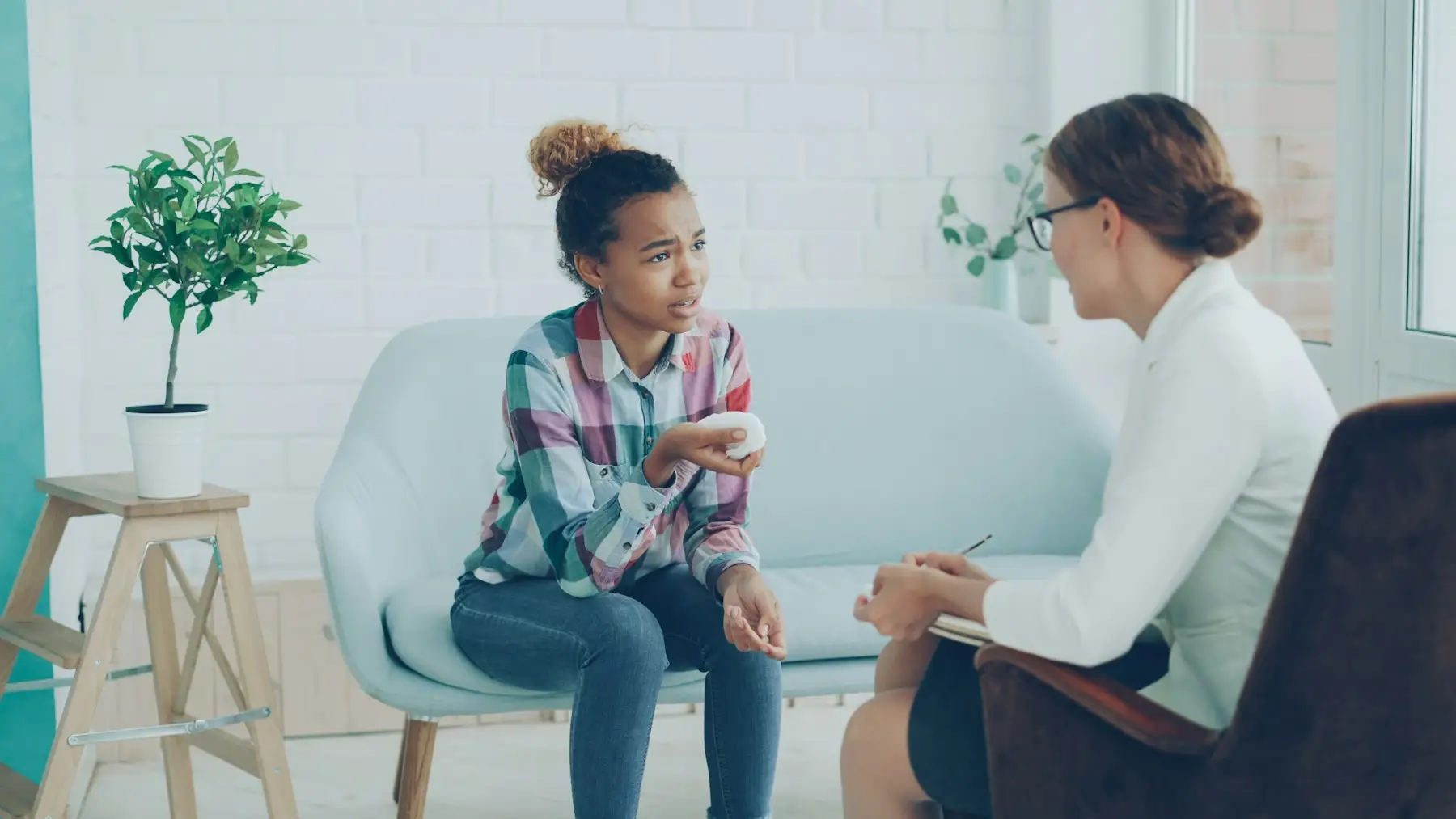 Jovem conversando com uma psicóloga em um consultório claro, sentadas frente a frente