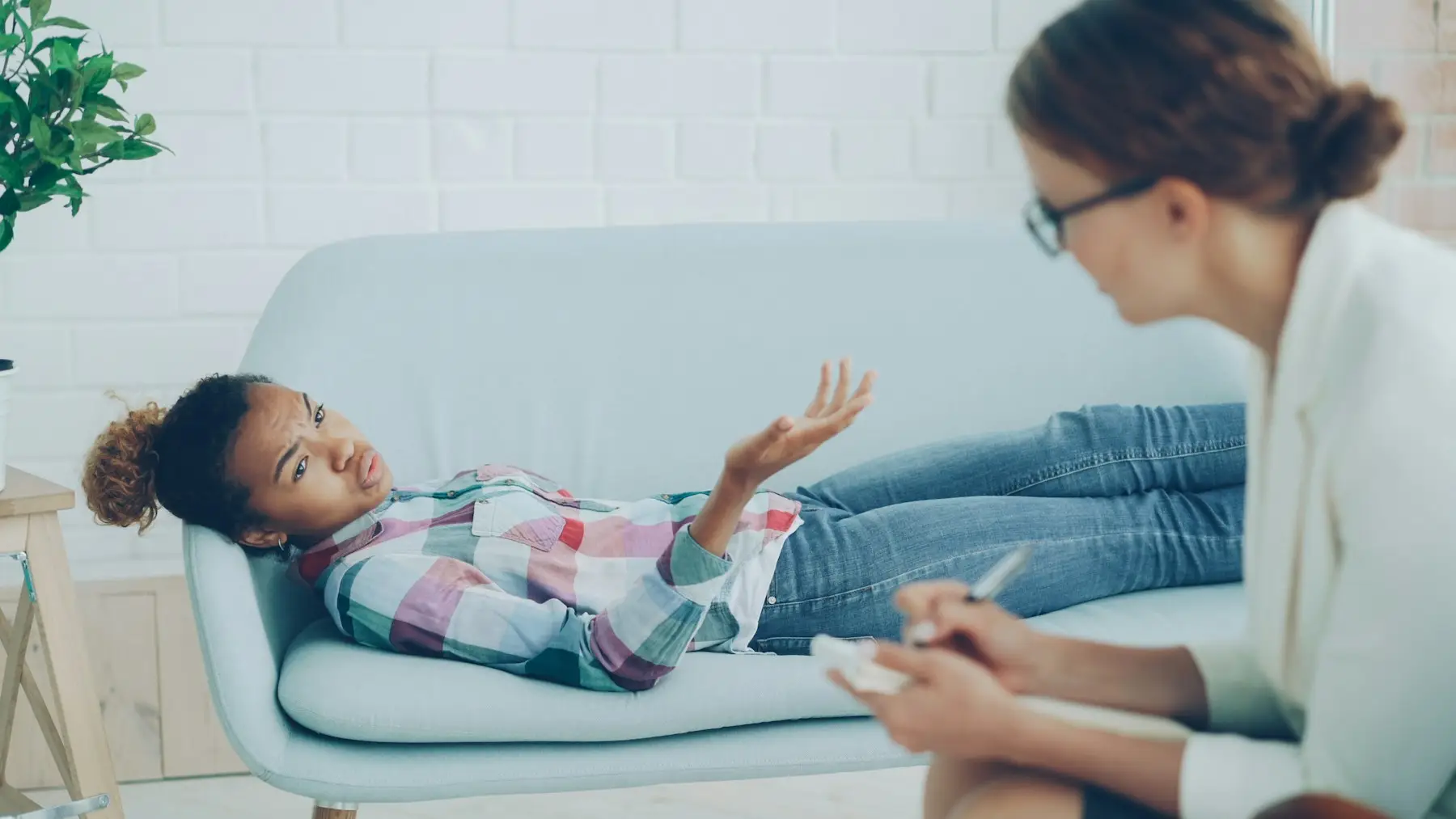 Paciente deitada no divã conversando com a psicóloga, que toma notas