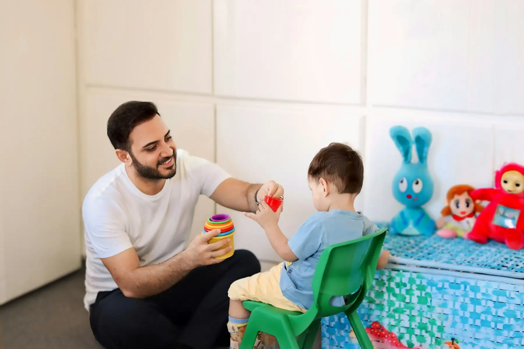 Terapeuta brincando com um menino pequeno em uma sala com brinquedos